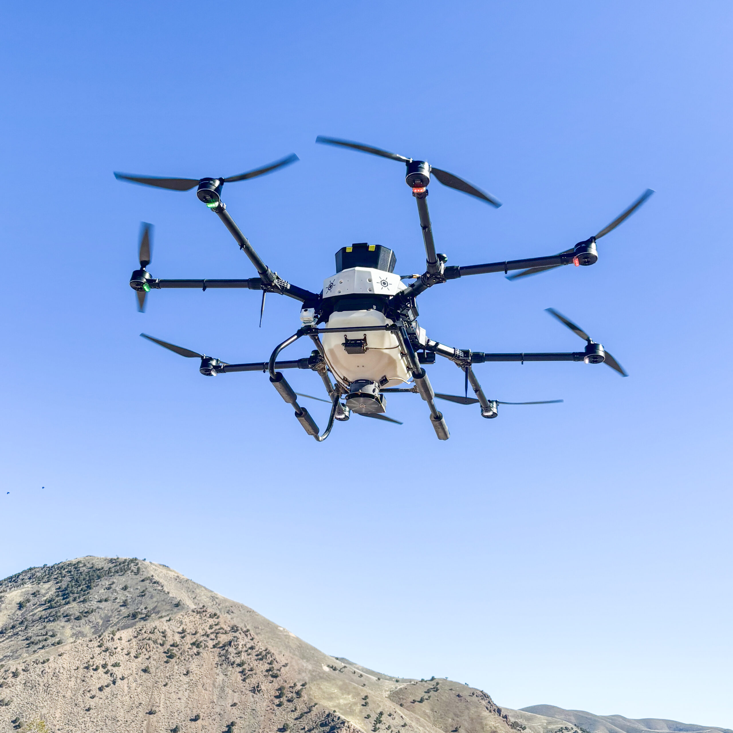 A drone flies above the camera, with a clear blue sky and mountains in the background